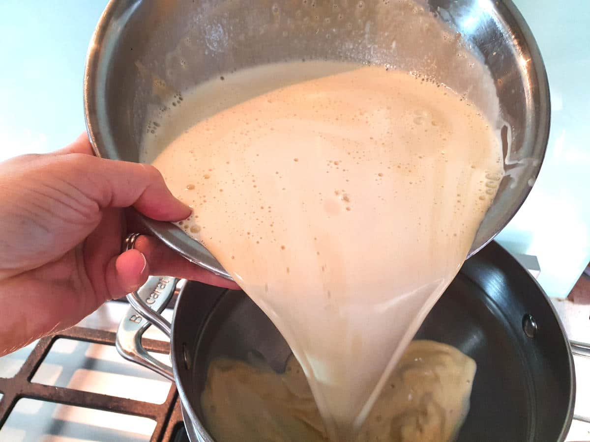 adding warm cream, brown sugar and egg yoke mix from a metal bowl into a double boiler, on a gas stove.