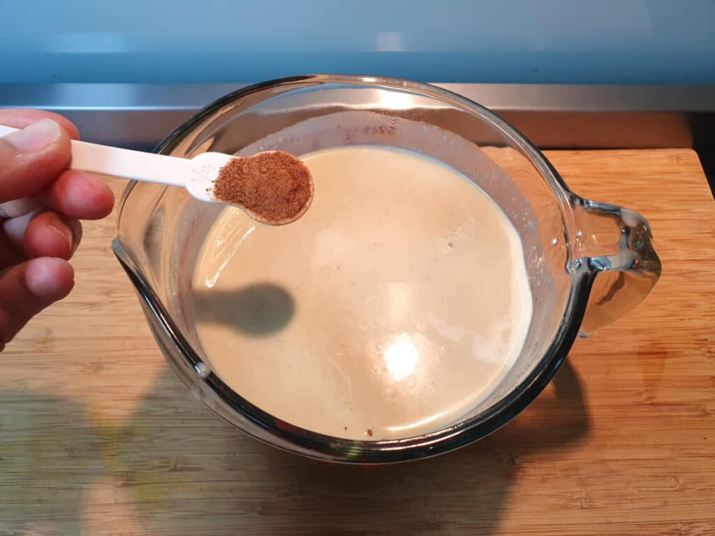 adding nutmeg to banana ice cream mix in glass jug on a chopping board.