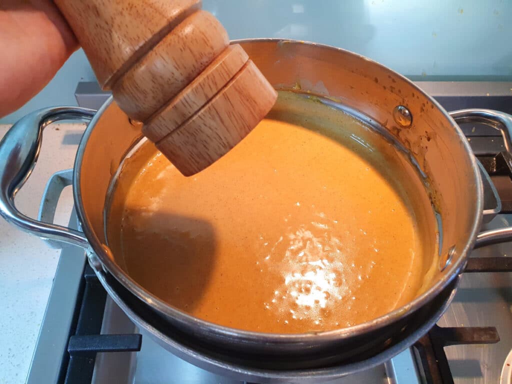 adding salt from salt grinder to pumpkin spice ice cream mix in a double boiler, on a gas stove.