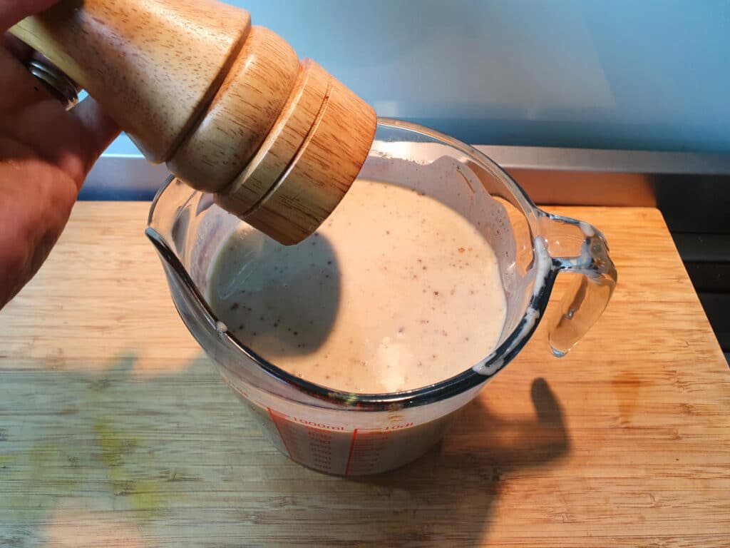 adding salt from salt grinder to banana ice cream mix in glass jug on a chopping board.