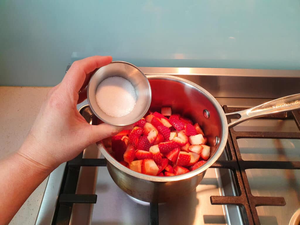 adding sugar to strawberries in pot on stove.