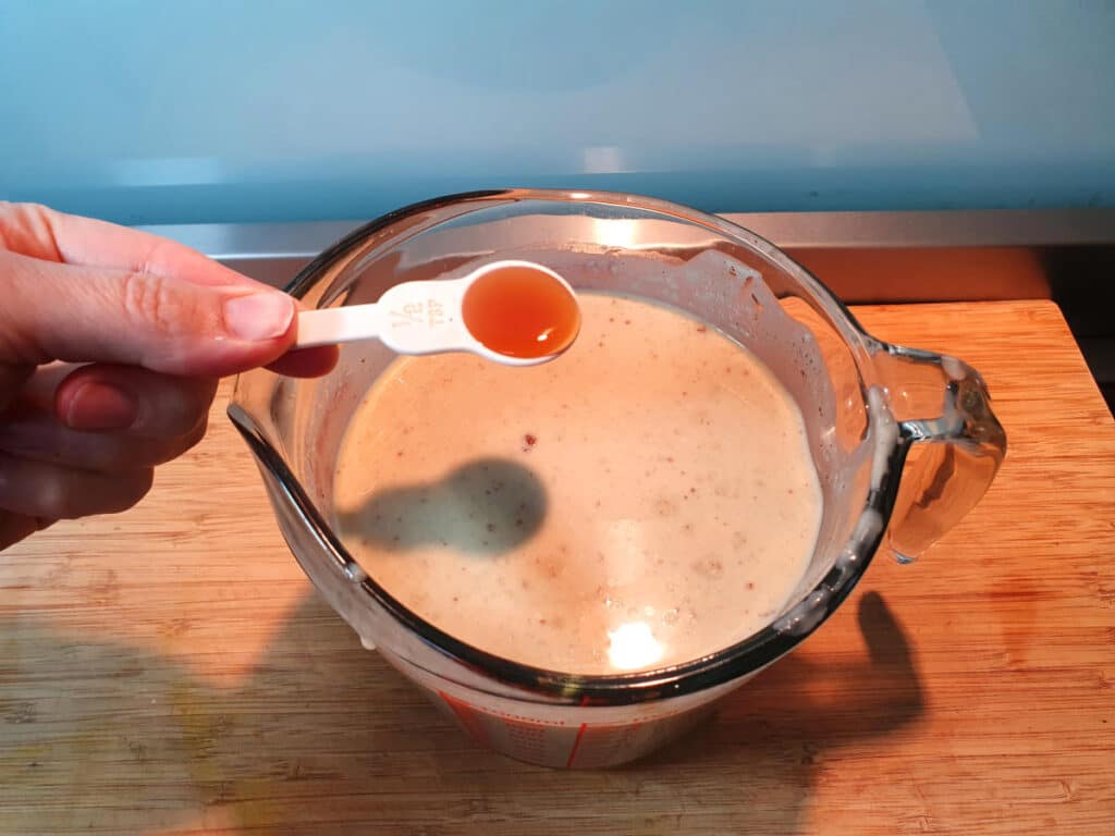 adding vanilla essence to banana ice cream mix in glass jug on a chopping board.