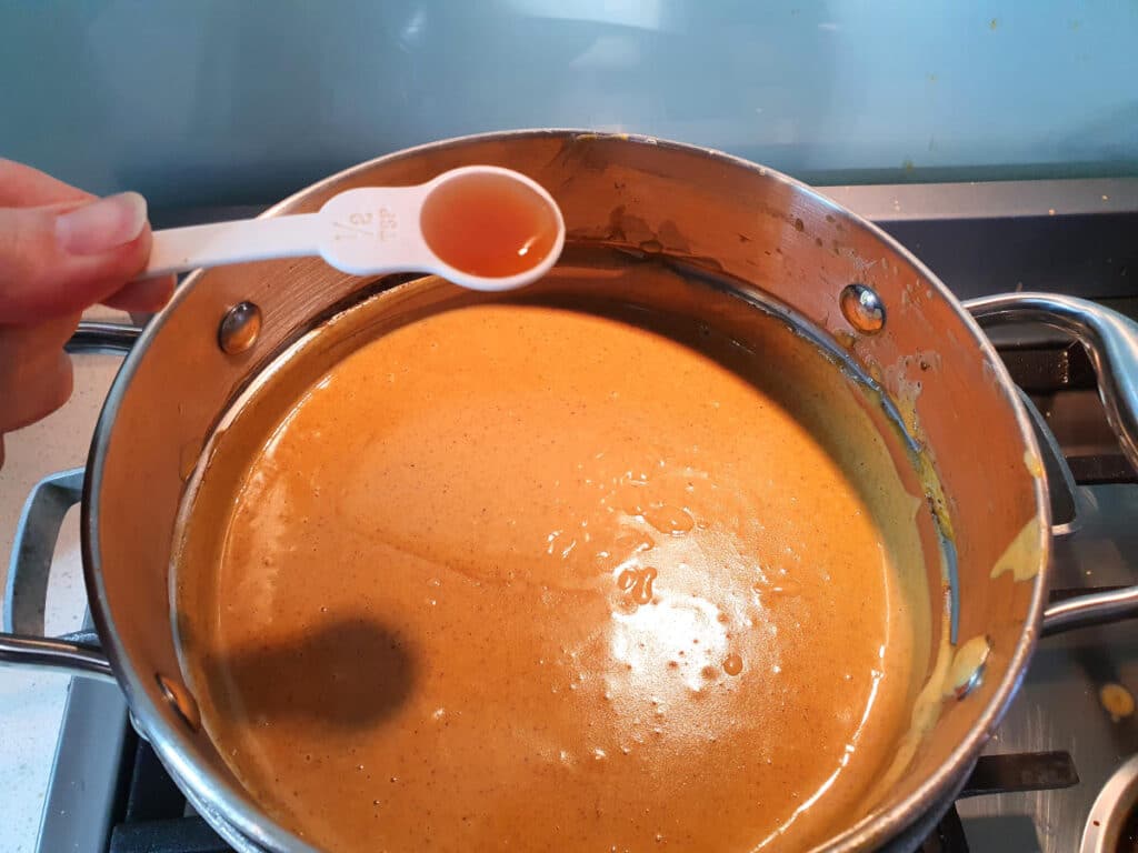 adding vanilla essence to pumpkin spice ice cream mix in a double boiler, on a gas stove.