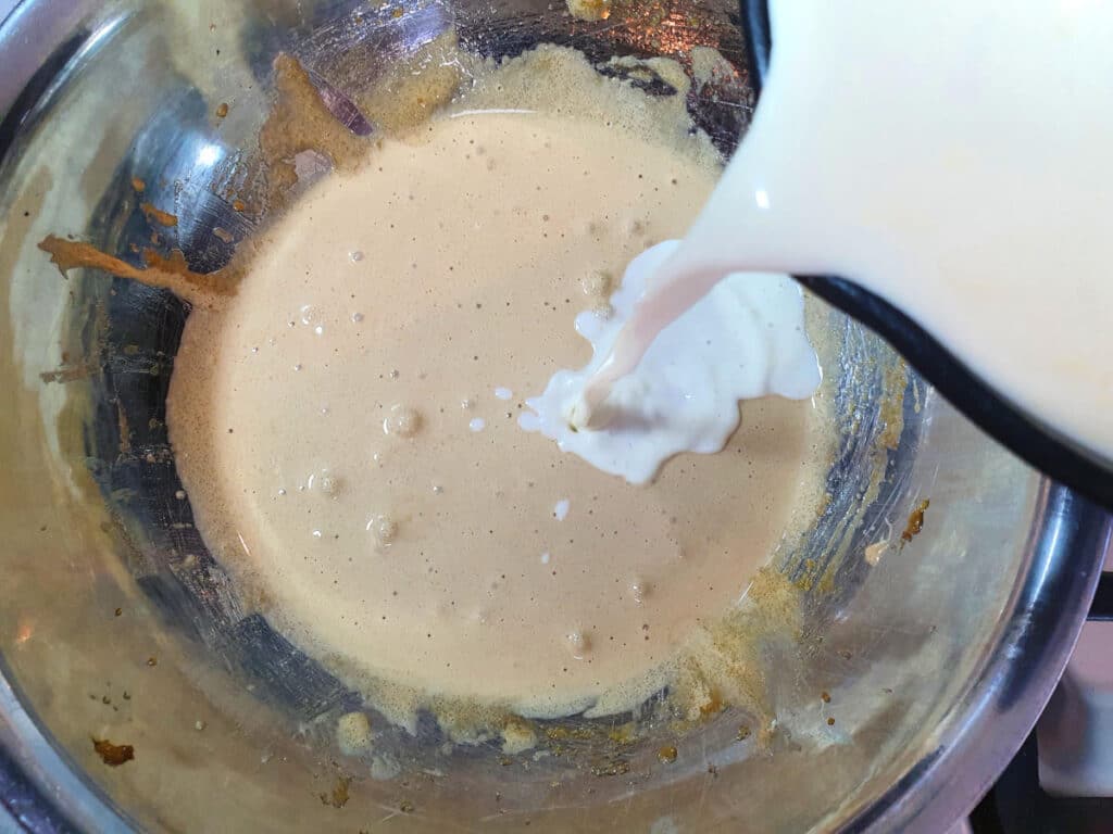 Top down view of pouring warmed cream to blended egg yoke and brown sugar mix, in a metal bowl.