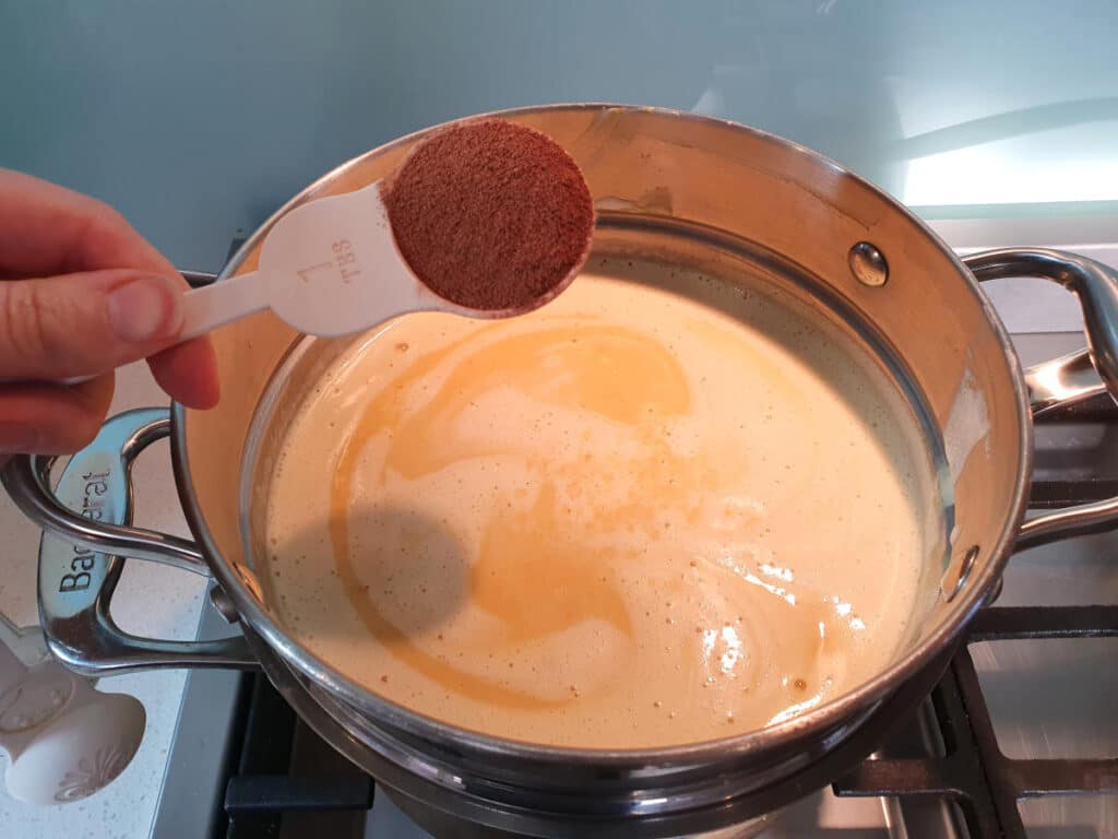 Adding spice mix to pumpkin spice ice cream mix in double boiler on a gas stove.