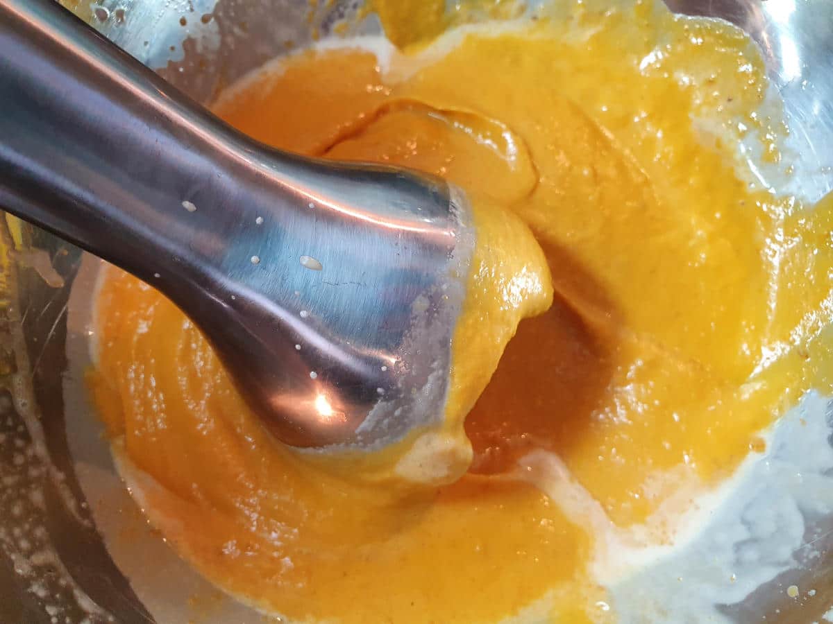 close up blending roasted pumpkin in a metal bowl with an immersion blender.