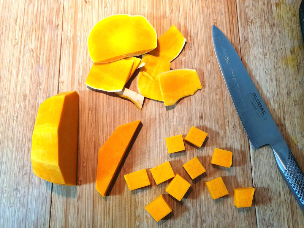 Pumpkin spice ice cream 5 Top down showing pumpkin chopped up at various of chopping, with a large knife, on a chopping board.