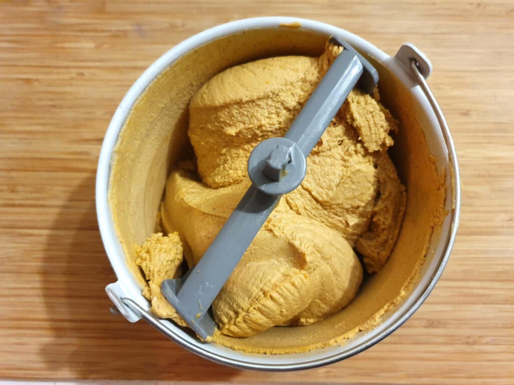 Top down view of churned pumpkin spice ice cream in churning bowl, on a chopping board.