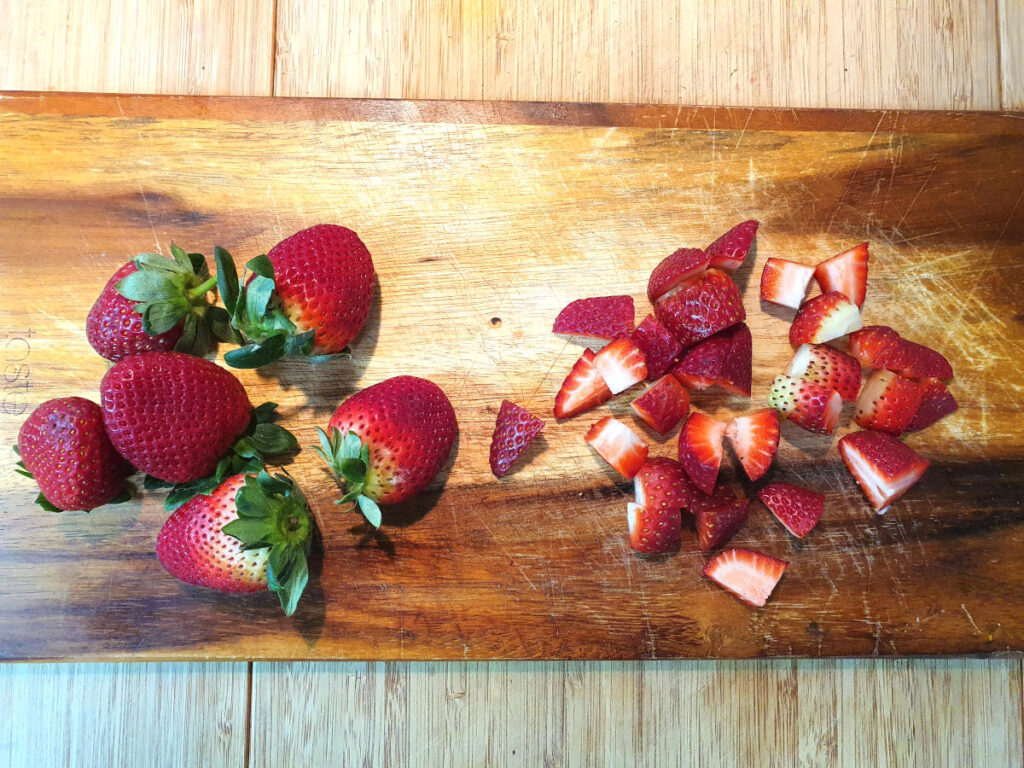 Strawberry compote (strawberry sauce) 3 cutting up strawberries on a chopping board.