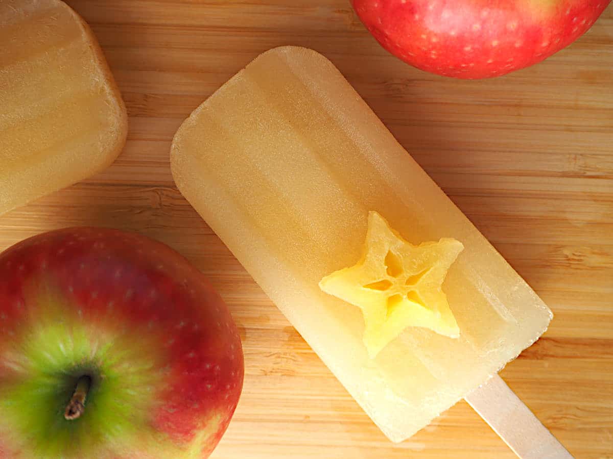 Mulled apple cider popsicles 16 Single mulled apple cider popsicle with apple star on top and apples, on a chopping board.