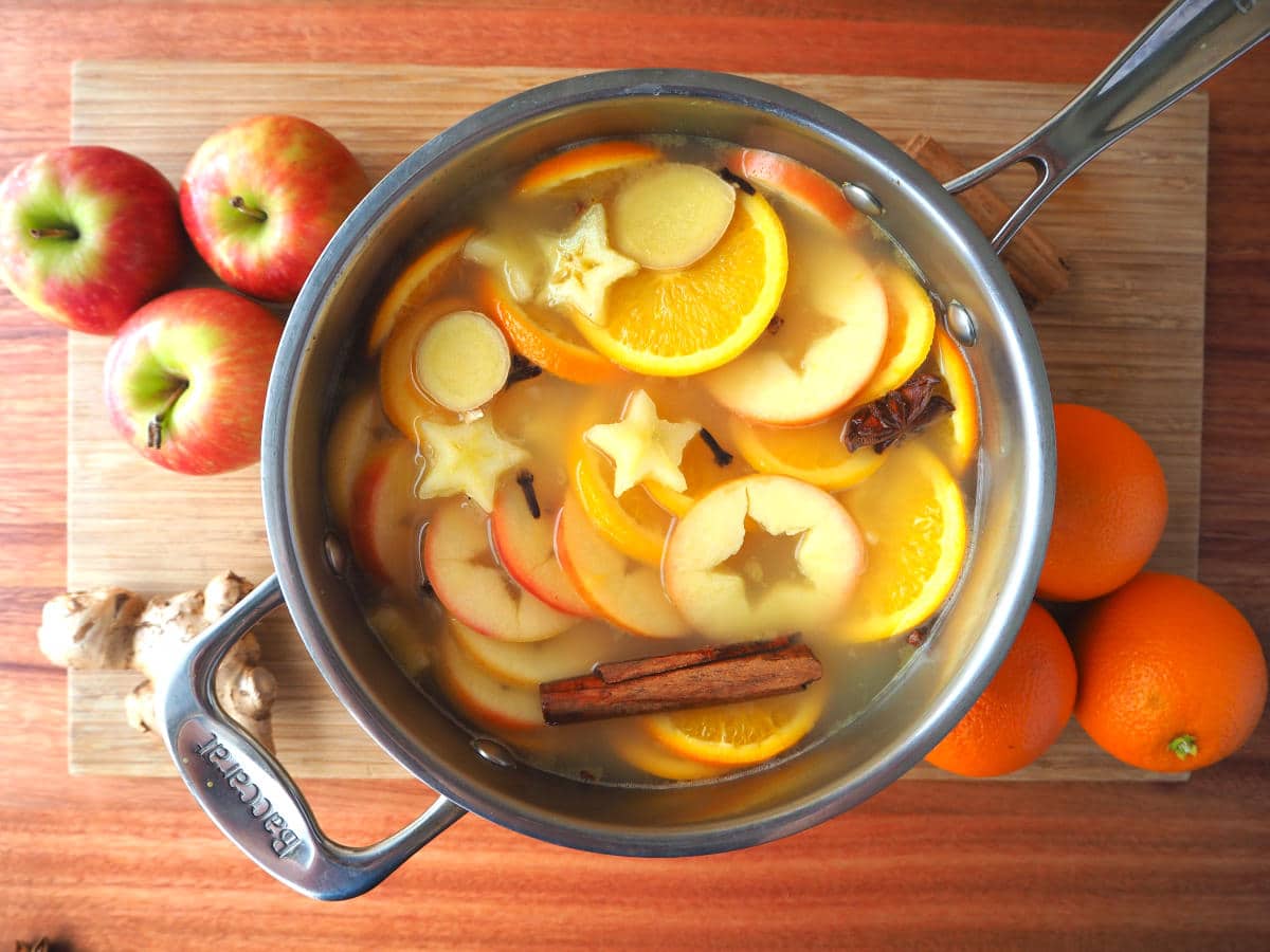 top down view of pot of mulled apple cider on a chopping board, with apples, oranges and ginger root on the side.