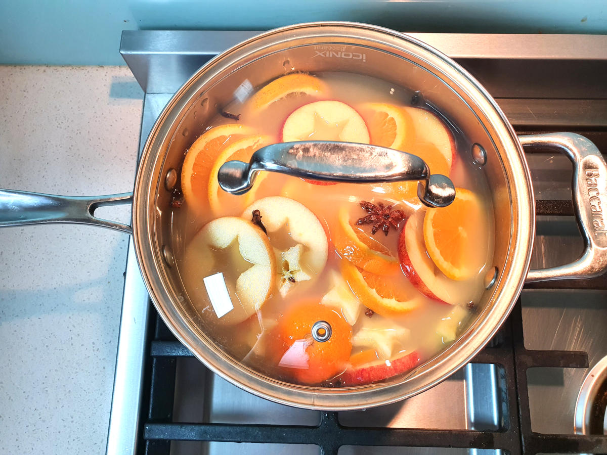 mulled apple cider with simmering in pot with clear glass lid, on a gas stove.