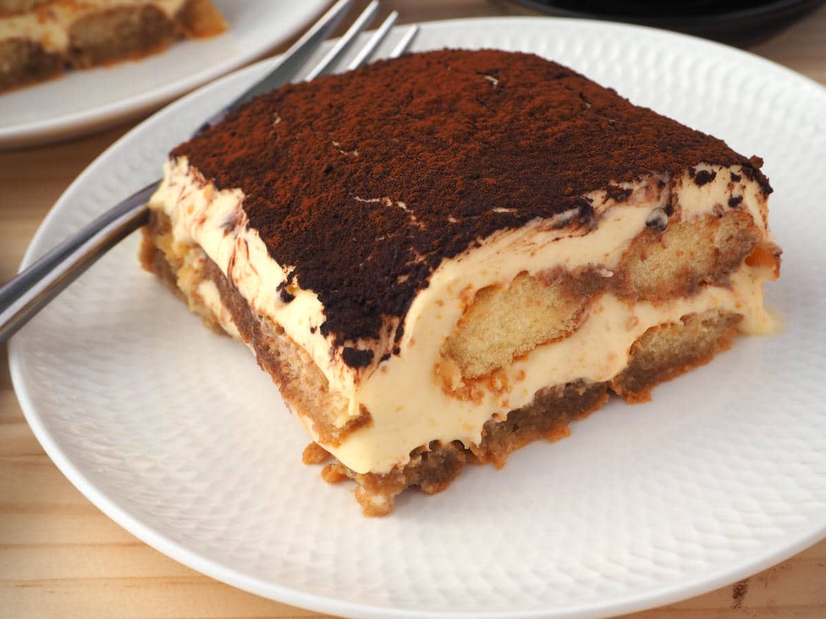 close up of diagonal view of pice of tiramisu on white plate with a fork.