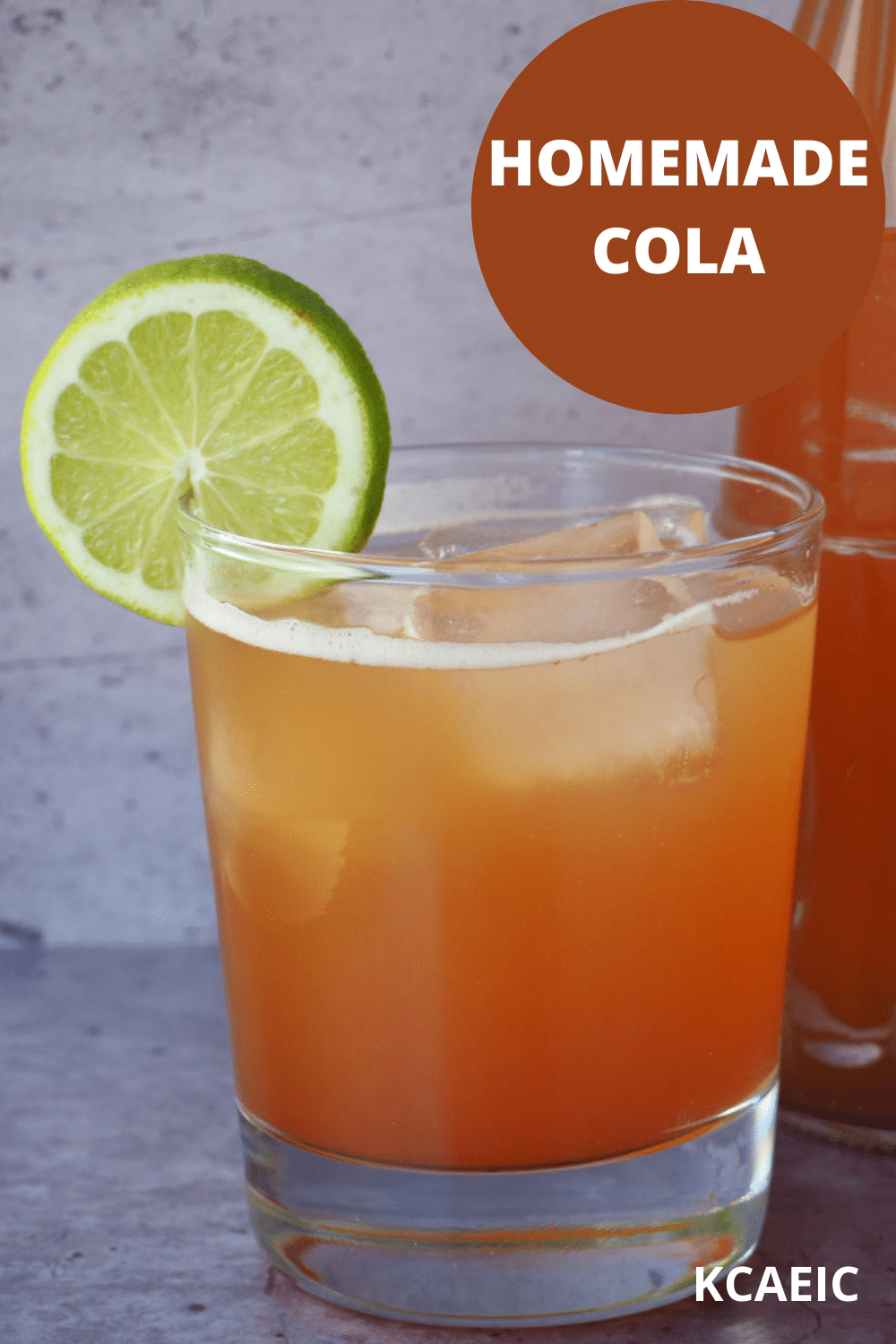 Glass of homemade cola with ice, lime circle garnish and bottle of cola beside it and text overlay, homemade cola, KCAEIC.