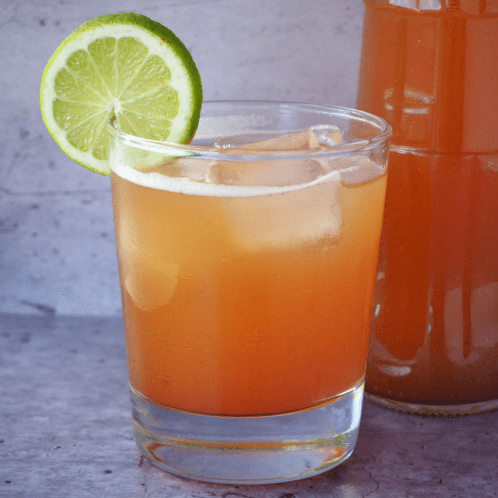 Glass of homemade cola with ice, lime circle garnish and bottle of cola beside it.