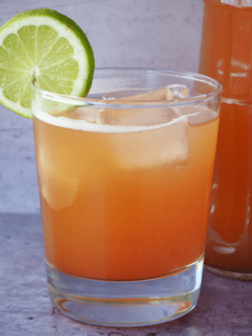 Glass of homemade cola with ice, lime circle garnish and bottle of cola beside it.