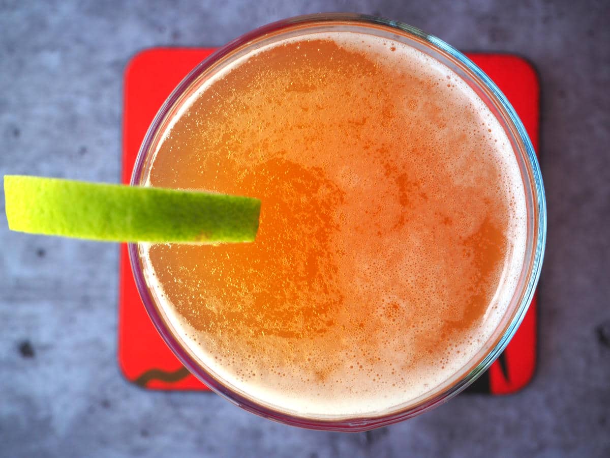 Top down view homemade cola in glass with lime circle garnish on side, with a red coaster under the glass.