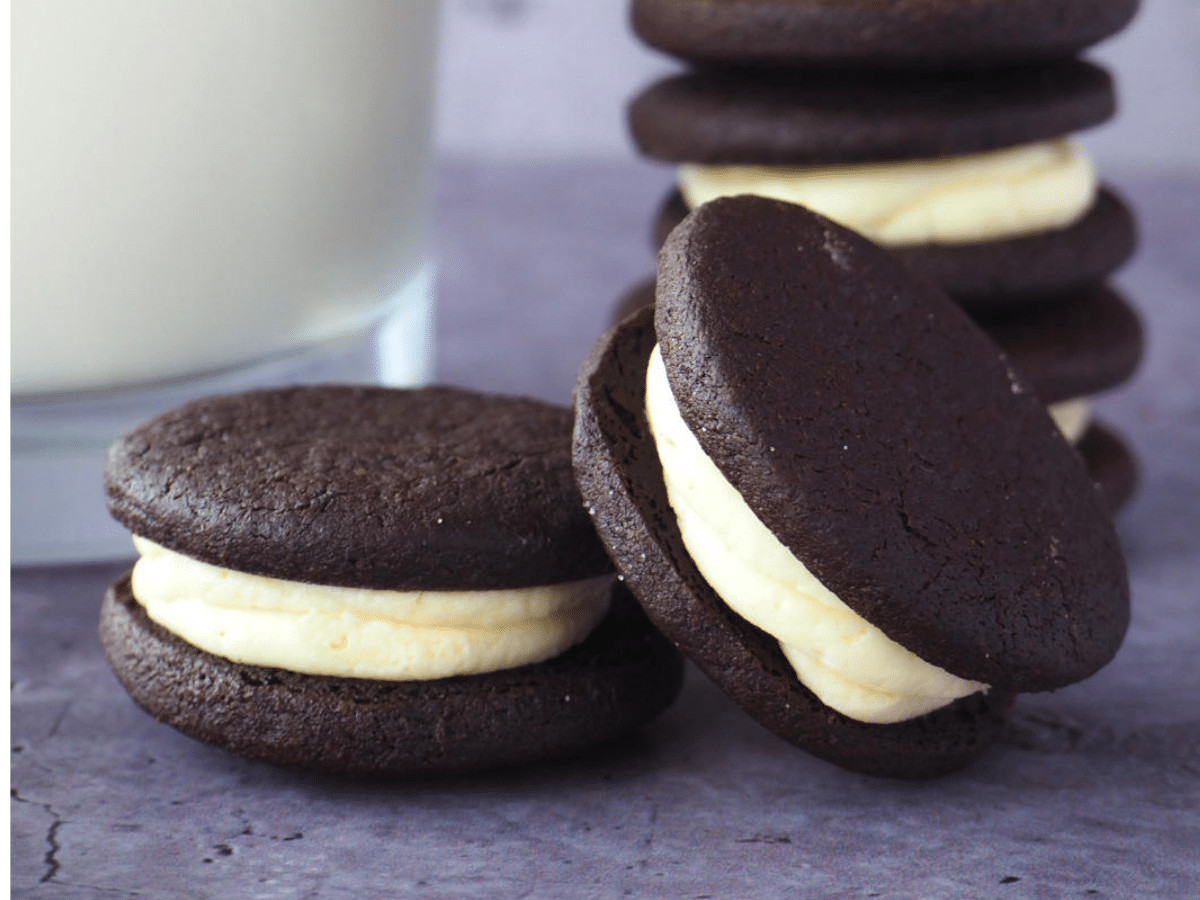 side view close up of two oreos, one proped on the other, with stack of homemade oreos, with glass of milk.