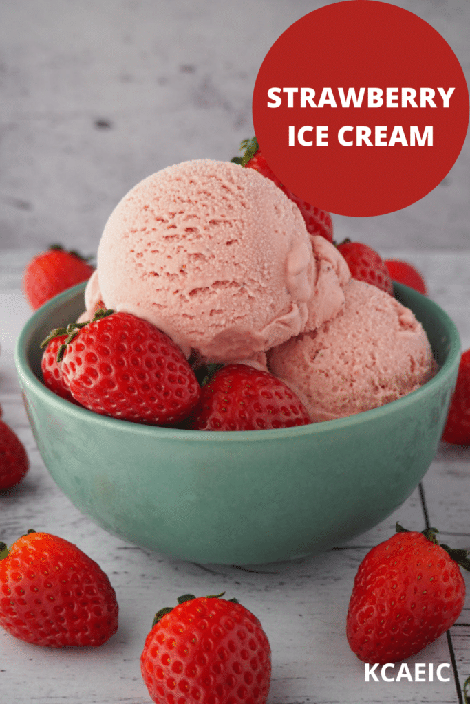 45 degree view of scoops of strawberry ice cream in a green bowl with strawberries in the bowl and strawberries scattered around it, on a white background, with text overlay, strawberry ice cream and KCAEIC.