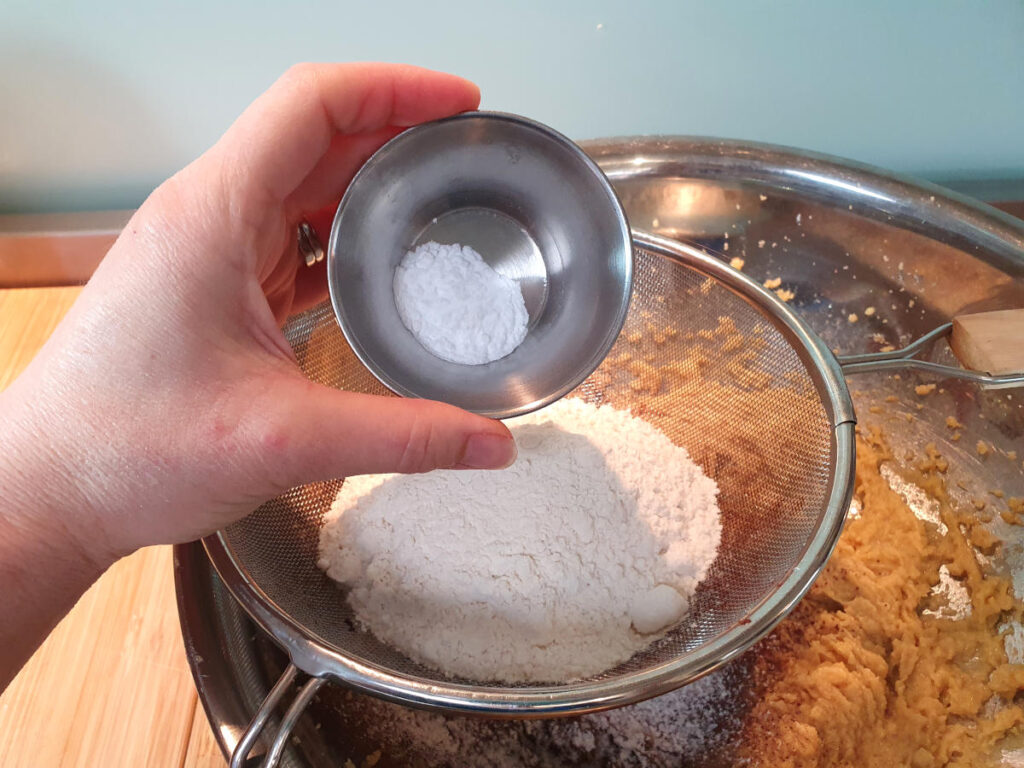 adding baking soda to other dry ingredients in sieve sittnig on top of mixing bowl with beaten wet ingredients.