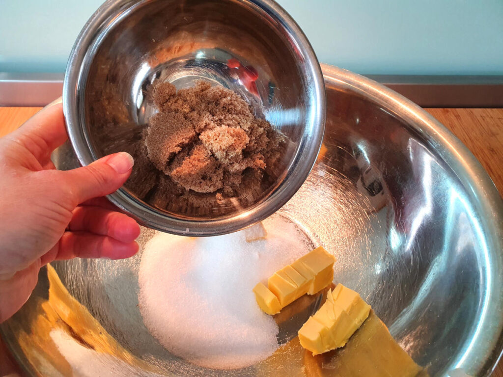 adding brown sugar to bowl with white sugar and butter in a large metal mixing bowl.