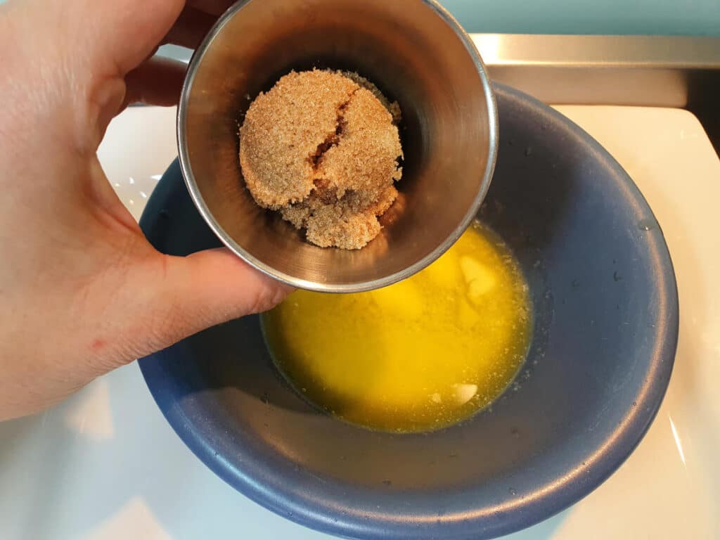 adding brown sugar to melted butter in a blue bowl.