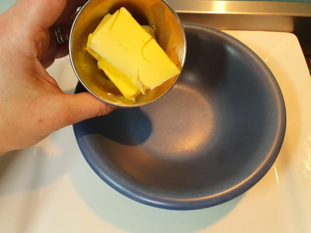 adding butter to a microwave blue bowl to melt in microwave.