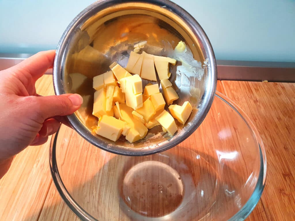 adding chopped room temperature butter to glass mixing bowl.