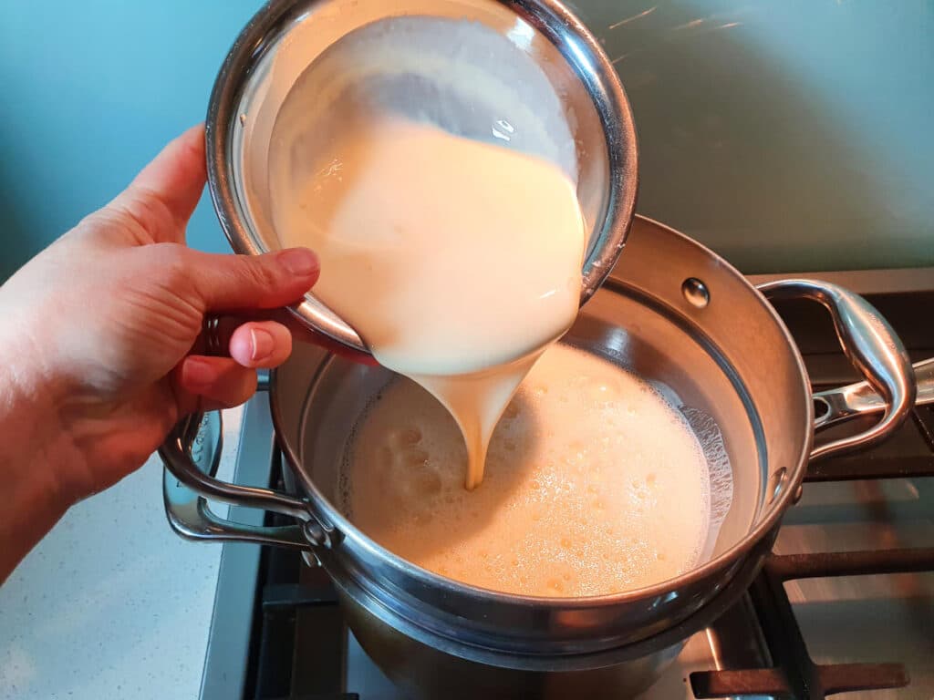 Adding cream to egg yoke, sugar and milk mix in double boiler on stove.