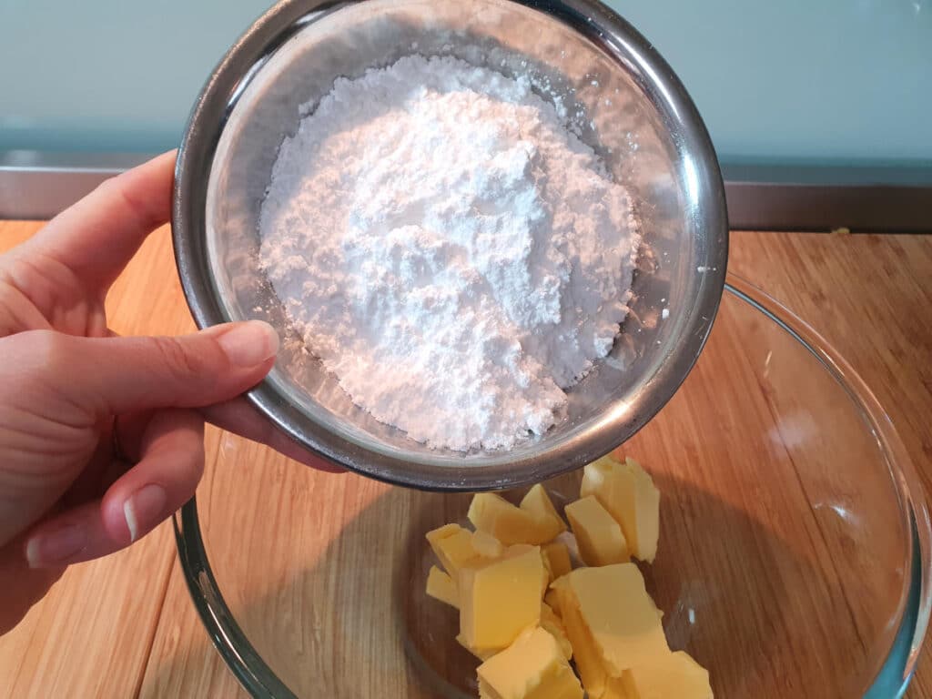 adding icing sugar to chopped butter in mixing bowl.