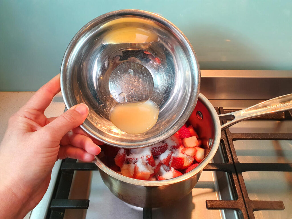 adding lemon juice to chopped strawberries in pot.