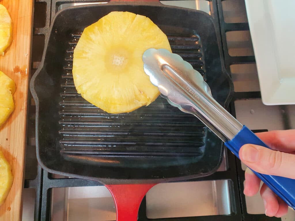 adding sliced pineapple to hot griddle pan.