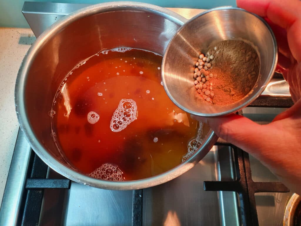 Homemade cola 12 adding small bowl of measured spices to saucepan.