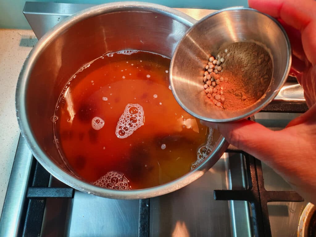 adding small bowl of measured spices to saucepan.