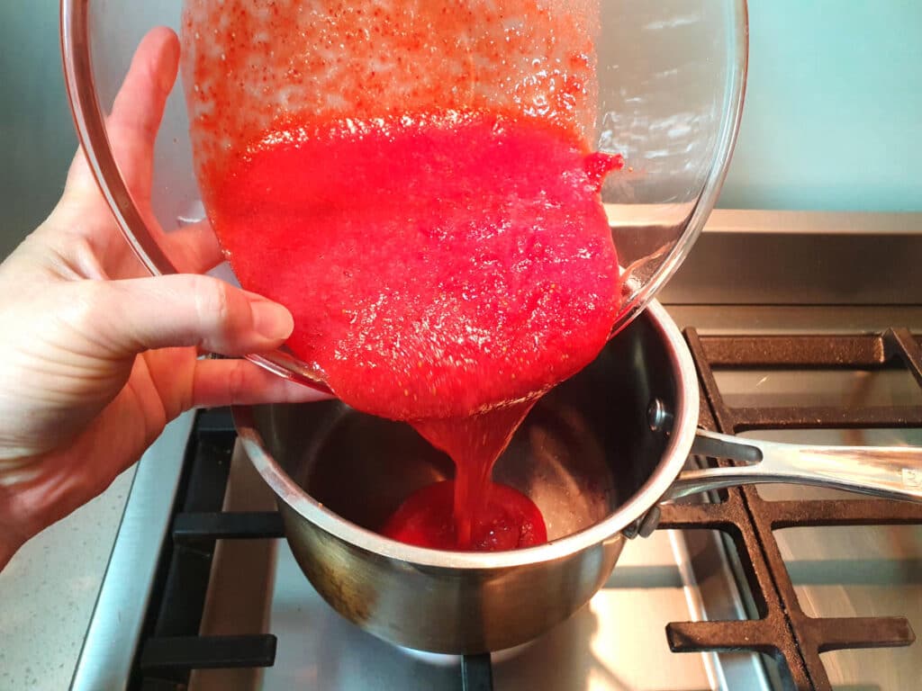 adding blitzed strawberries to pot on stove.