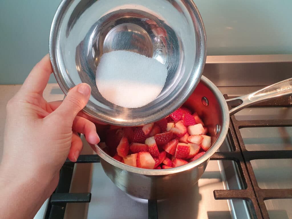 Adding sugar to strawberries in pot.