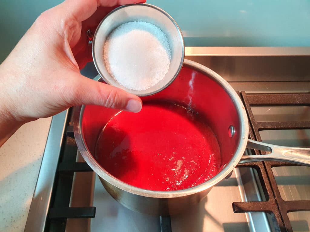 adding sugar to strawberry mix in pot on stove.