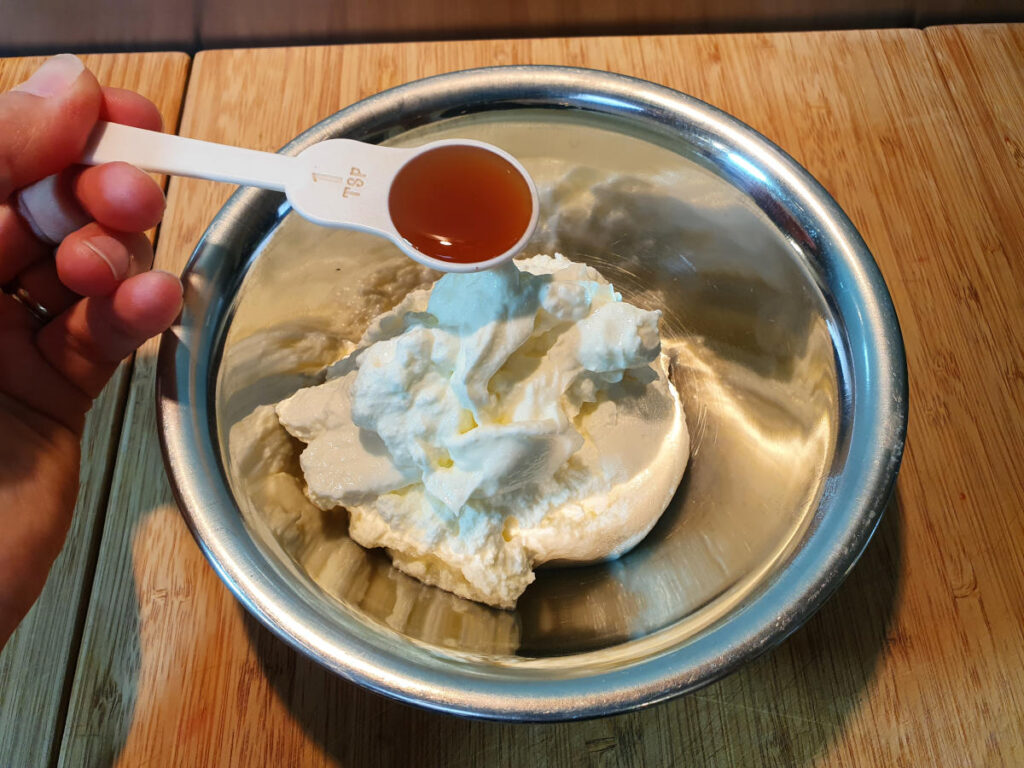 adding vanilla to bowl with Greek yogurt.