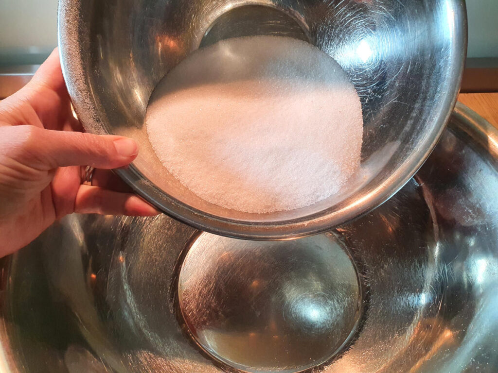 adding white sugar to a large metal mixing bowl.