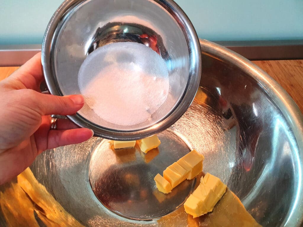 adding white sugar to butting in a large metal bowl.