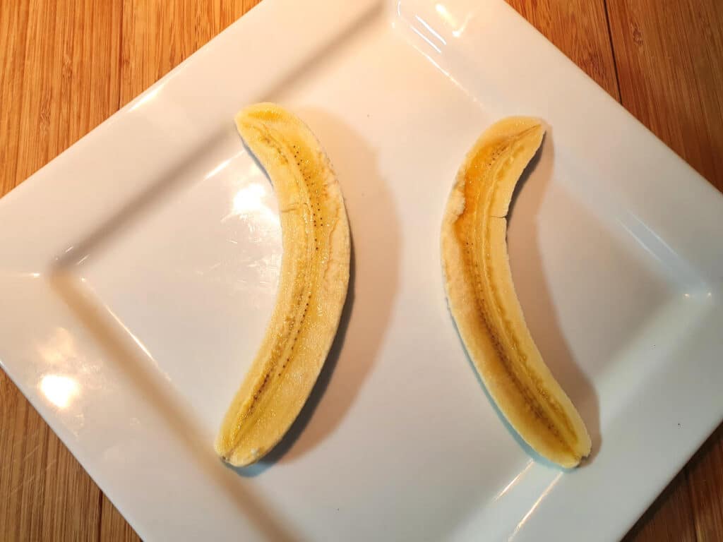 Banana split 5 putting two banana pieces on plate, curves facing outwards, with space inbetween for the ice cream.