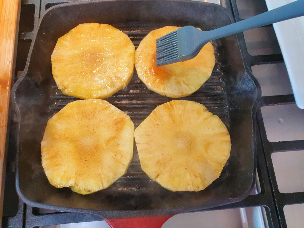 brushing other side cooking pineapple in griddle pan with butter, sugar, cinnamon mix.