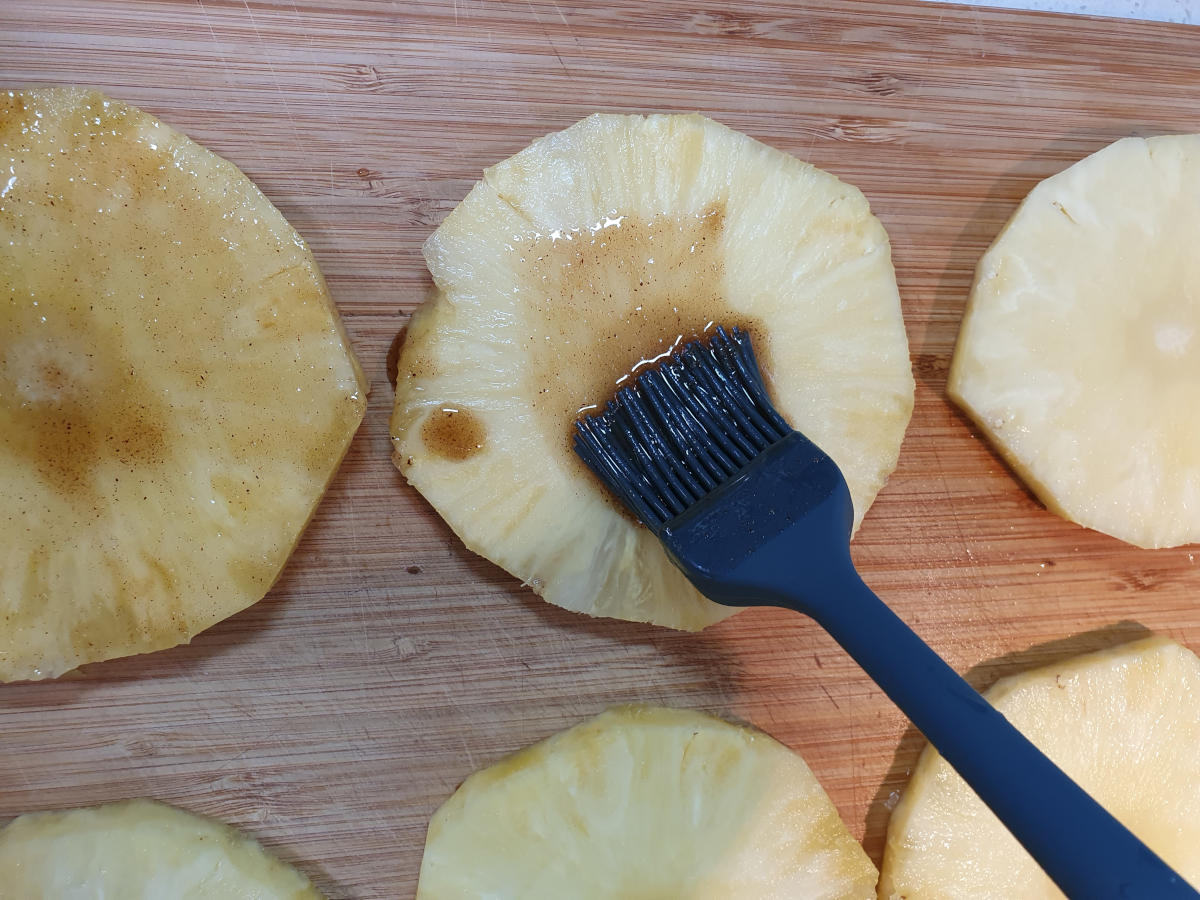 brushing laid out sliced pineapple with butter, sugar, cinnamon mix.
