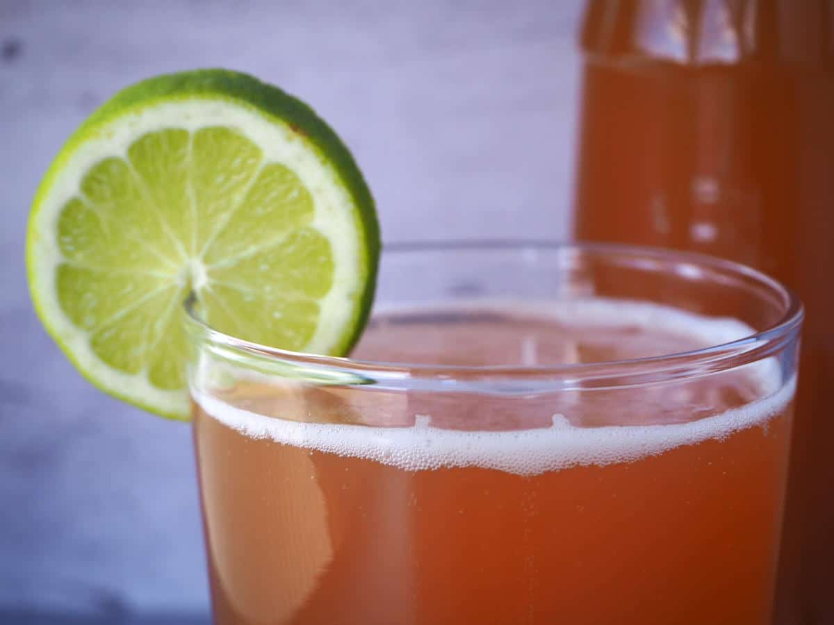 close up of glass of homemade cola with lime circle garnish and bottle of cola in background.