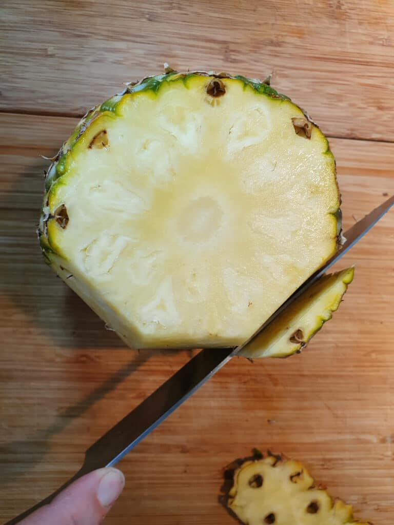 continuing to work around the pineapple turned up on its end, slicing the skin off with a shart knife.