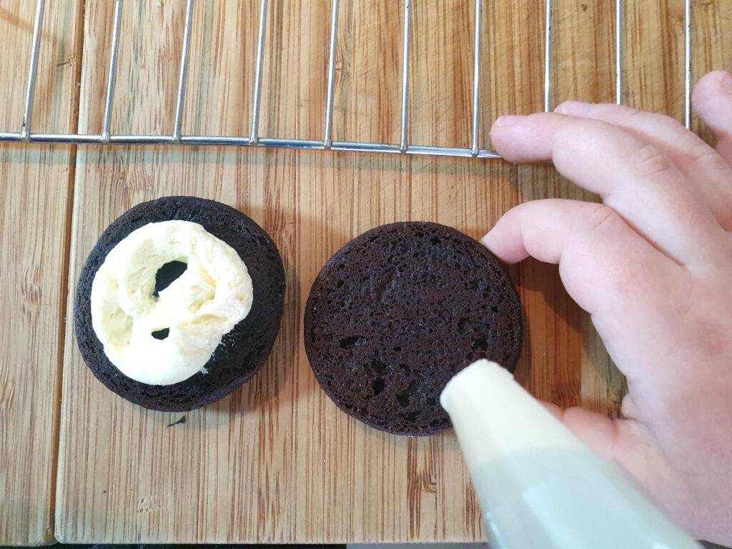 down down view filling oreos with vanilla butter filling in a piping bag.