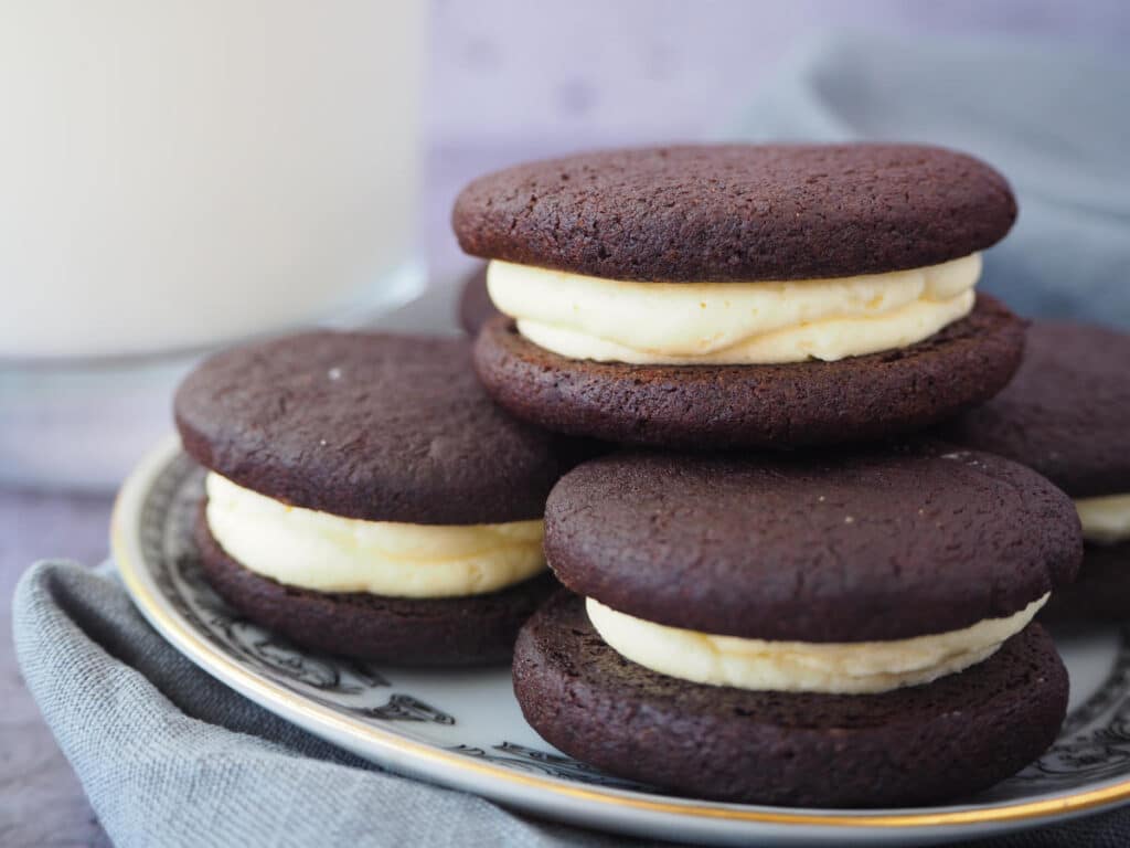 side view of homemade oreas stacked on a a white plate with a black border pattern and gold rim, on a grey tea towel and a glass of milk on the side.