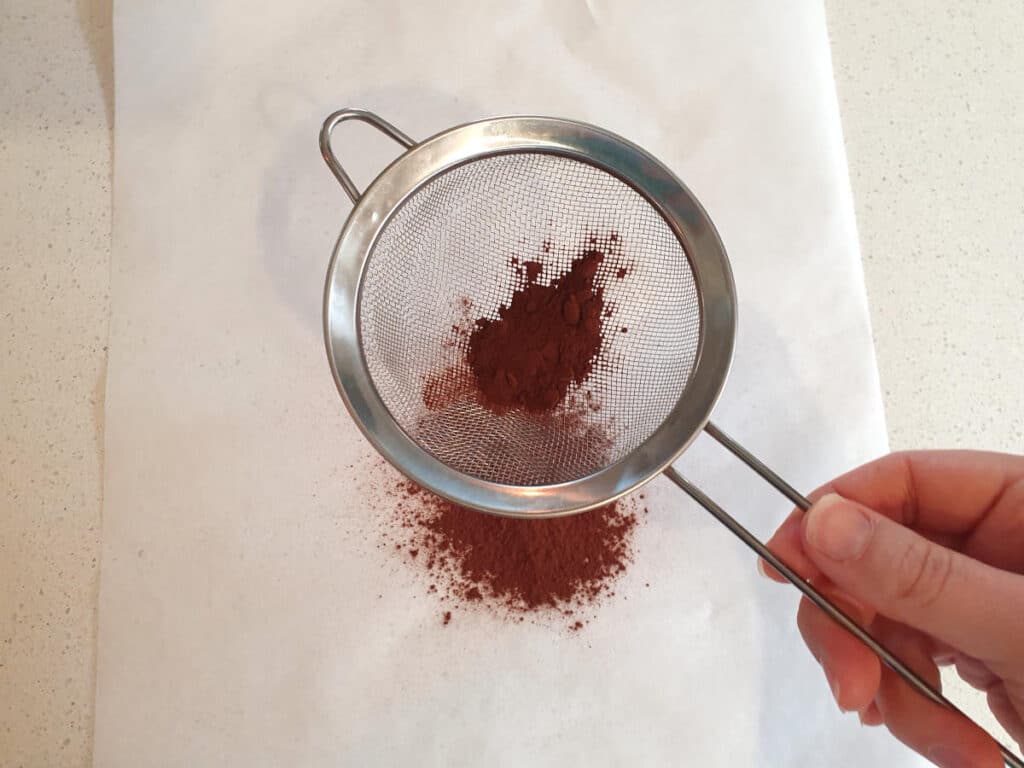 top down view sifting cocoa powder onto baking paper.