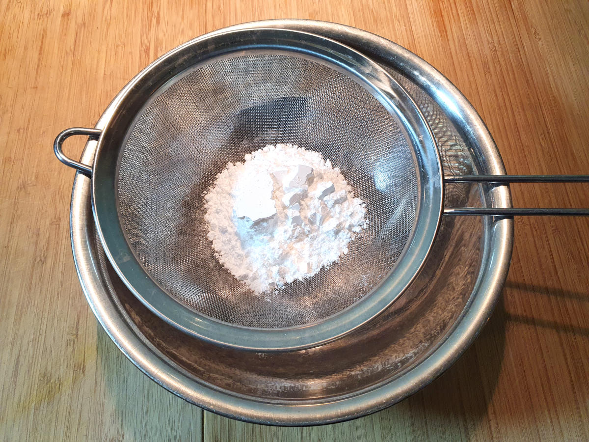 sifting icing sugar into a metal bowl.