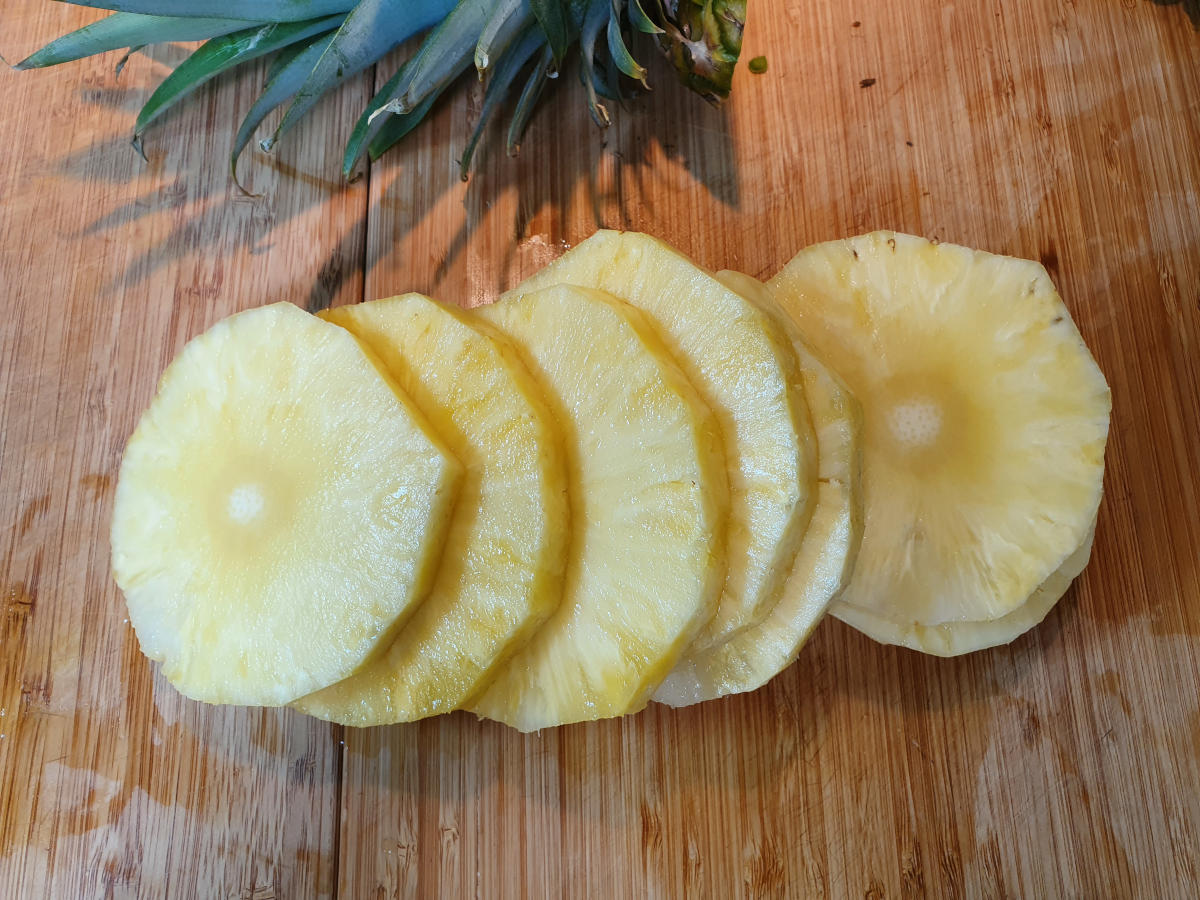 pineapple slices ready to be cooked, on a chopping board, with pineaple top to the side.